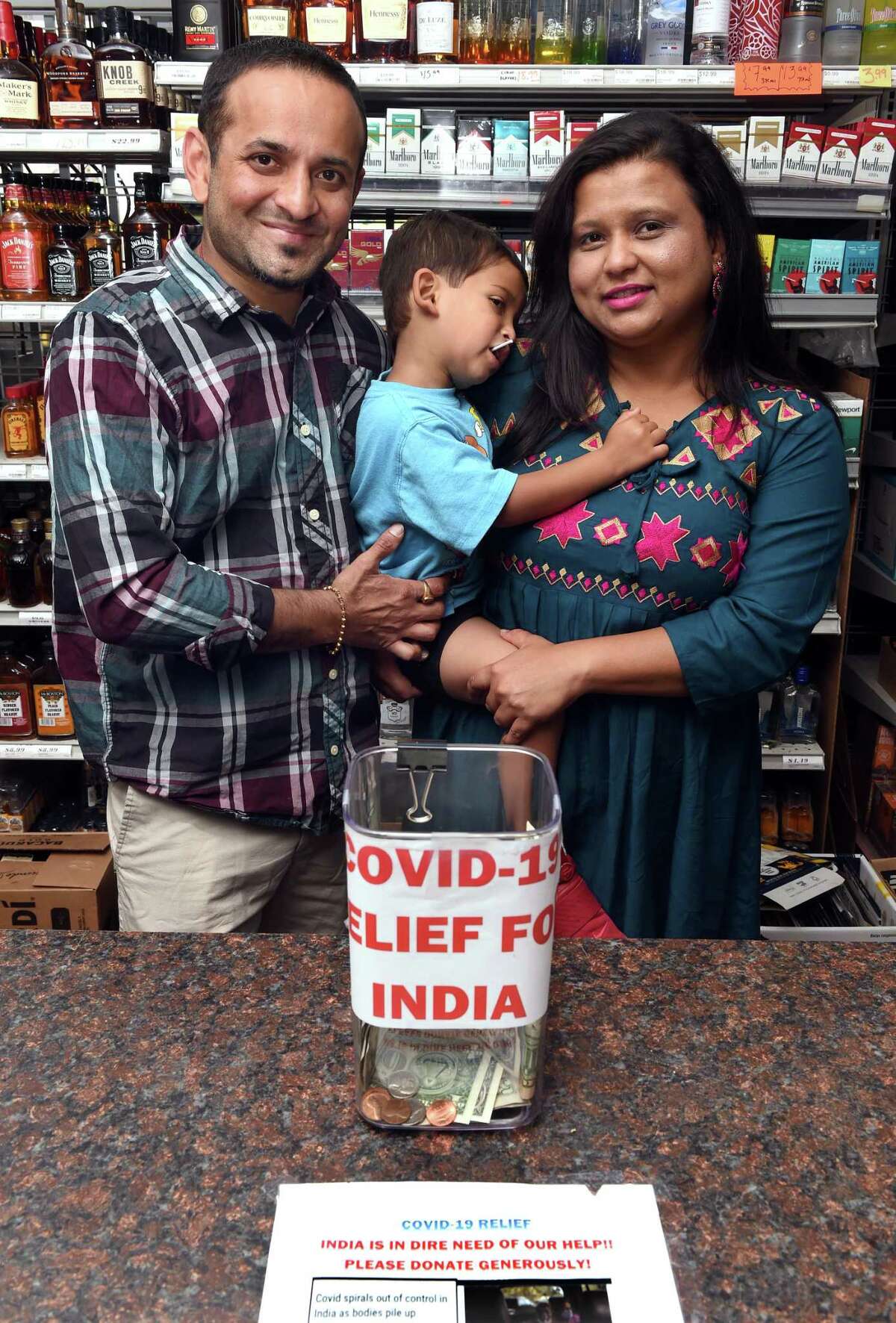 Keyur Patel, left, with his wife, Nital, and son, Ved, 31/2, behind the counter of one of the family’s package stores, Town & Country Liquors in Bethany, May 19, 2021, where he is raising funds and matching donations for COVID-19 relief in India.