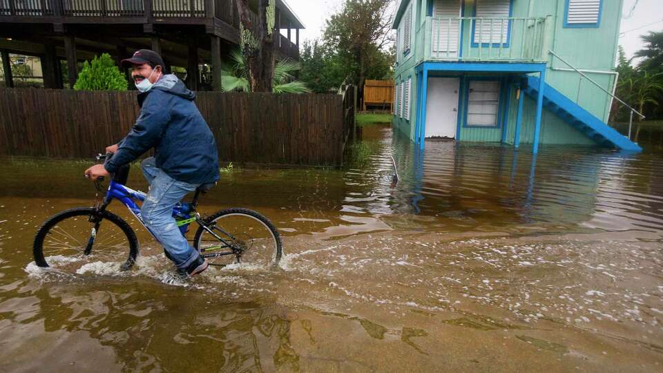 Rafael Juarez rides his bicycle through a street flooded by Tropical Storm Beta as he makes his way home from the store Monday, Sept. 21, 2020 in Galveston.