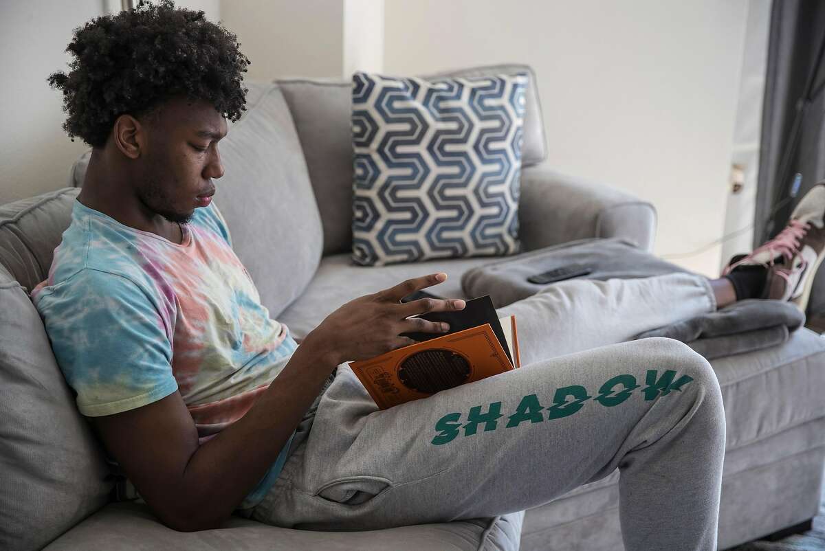 Golden State Warriors rookie, James Wiseman reads from the, "Wizenard Series Season One" book in his apartment in San Francisco, Calif., on Sunday, March 28, 2021. Wiseman is finding his way in his first season with the Warriors, but spends time at home practicing Mandarin, meditating, reading and creating beats. Photographer’s note: This photo was made from a remote camera held by Wiseman’s assistant inside the apartment while the photographer triggered the frame while looking at a computer outside to maintain NBA Covid precautions.