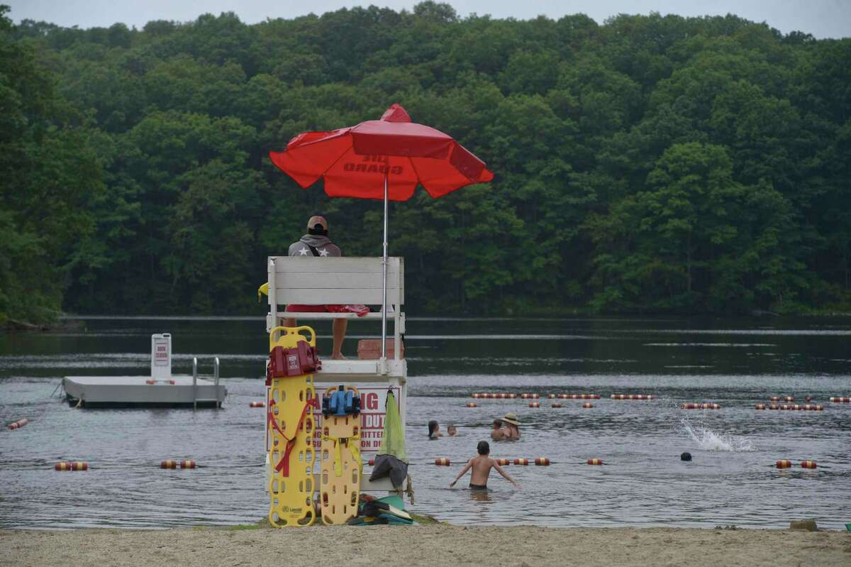 Head lifeguard Charlie Wilson of Easton, keeps an eye on swimmers at Topstone Park beach on Tuesday. The park and recreation department is loosening its reservation policy for residents looking to use the beach. Coronavirus restrictions are still in place. July 7, 2020, in Redding, Conn.