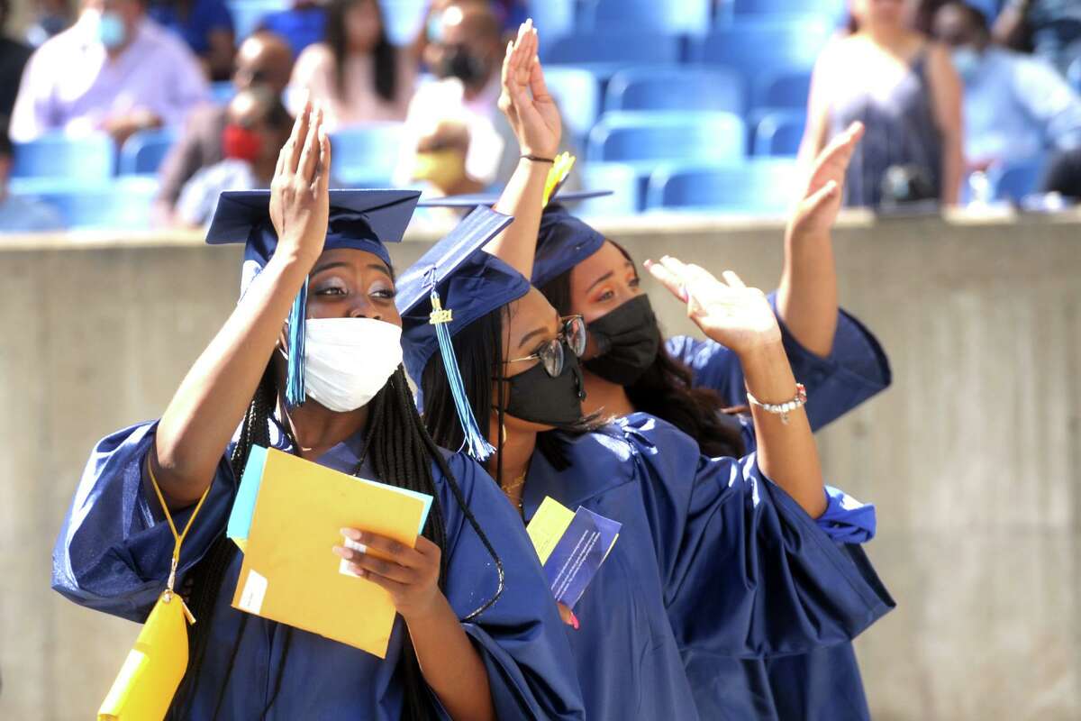 Three graduates wave to the crowd as they enter Hartford Healthcare Amphitheater for commencement of the Housatonic Community College class of 2021, in Bridgeport, Conn. May 27, 2021.