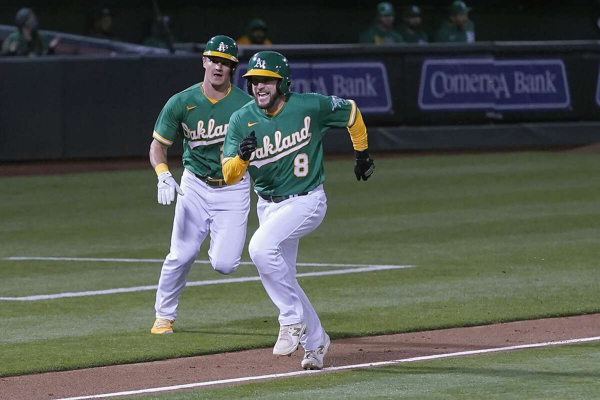 Jed Lowrie (8) and Matt Chapman head toward home plate to score on Sean Murphy’s single during the A’s five-run sixth inning at the Coliseum.