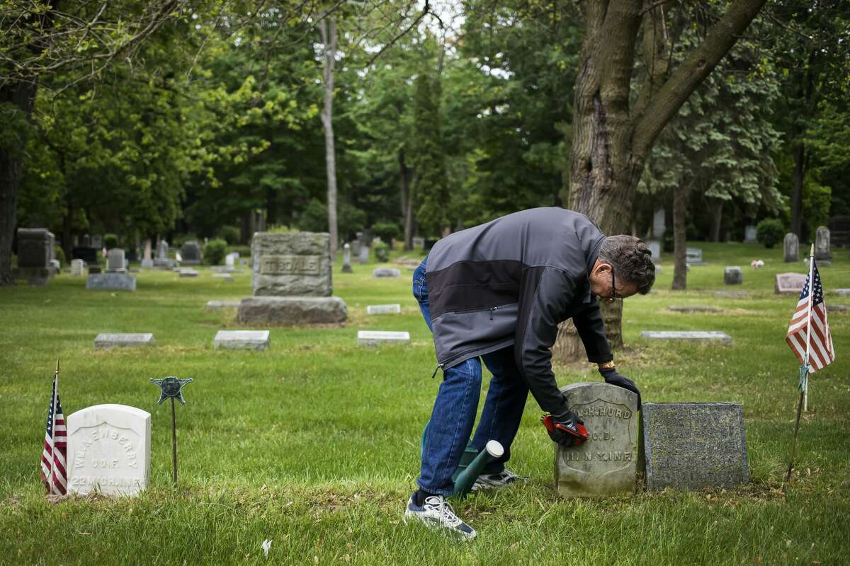 Floyd Andrick of the Midland County Historical Society begins the process of cleaning the headstone of civil war veteran William H. Hurd Thursday, May 27, 2021 in the Midland Municipal Cemetery. The headstone on the left was previously cleaned by Andrick. (Katy Kildee/kkildee@mdn.net)