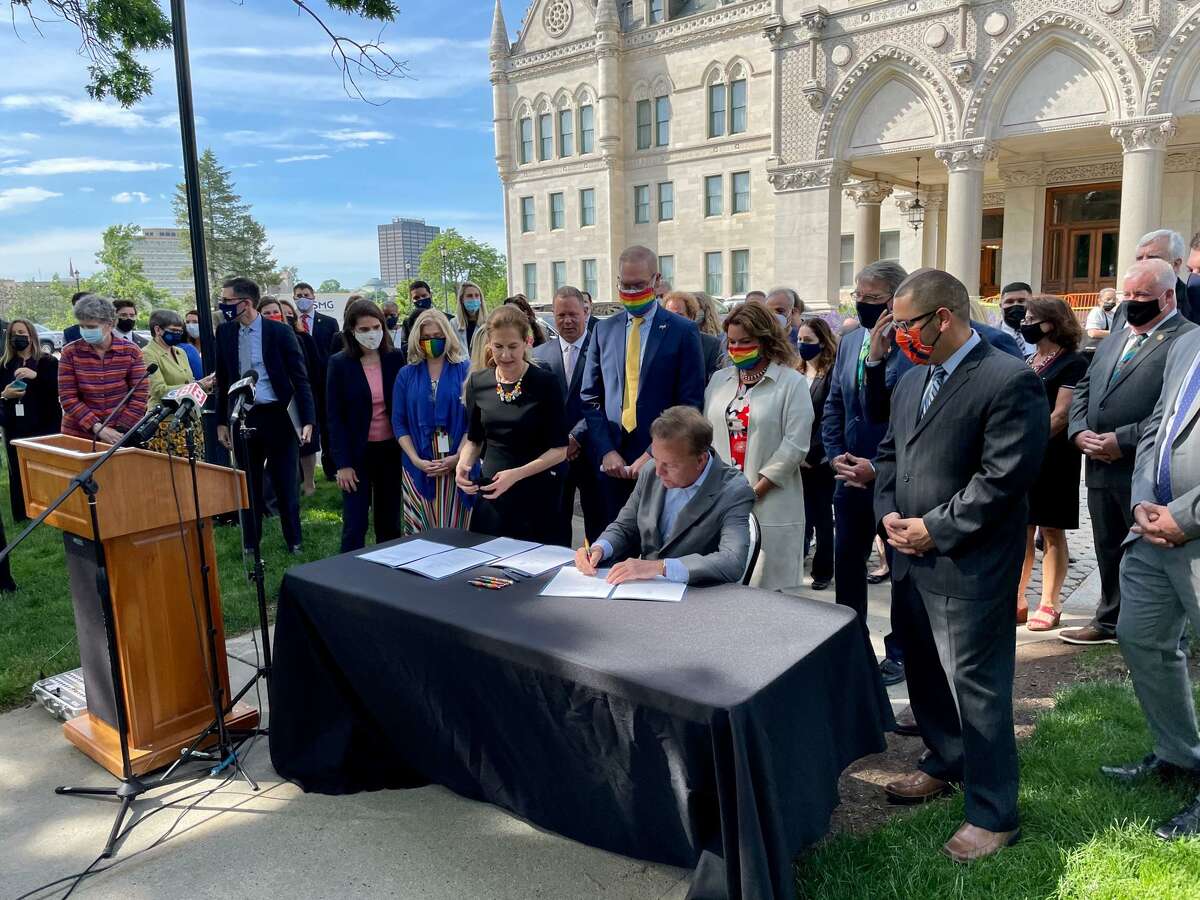 Gov. Ned Lamont signs a ceremonial copy of the Connecticut Parentage Act. Directly behind him are two key sponsors of the bipartisan bill, Reps. Jeff Currey, D-East Hartford, and Nicole Klarides-Ditria, R-Seymour.