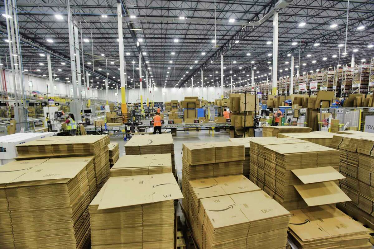 Stacks of boxes are seen in the foreground as employees work boxing up items for customers at the Amazon fulfillment center on Wednesday, June 2, 2021, in Schodack, N.Y. Computers inform workers which box to use for an item and a computer figures out the correct amount of tape needed to close the box. From the fulfillment center packages are sent to an Amazon sortation center or a delivery station. (Paul Buckowski/Times Union)