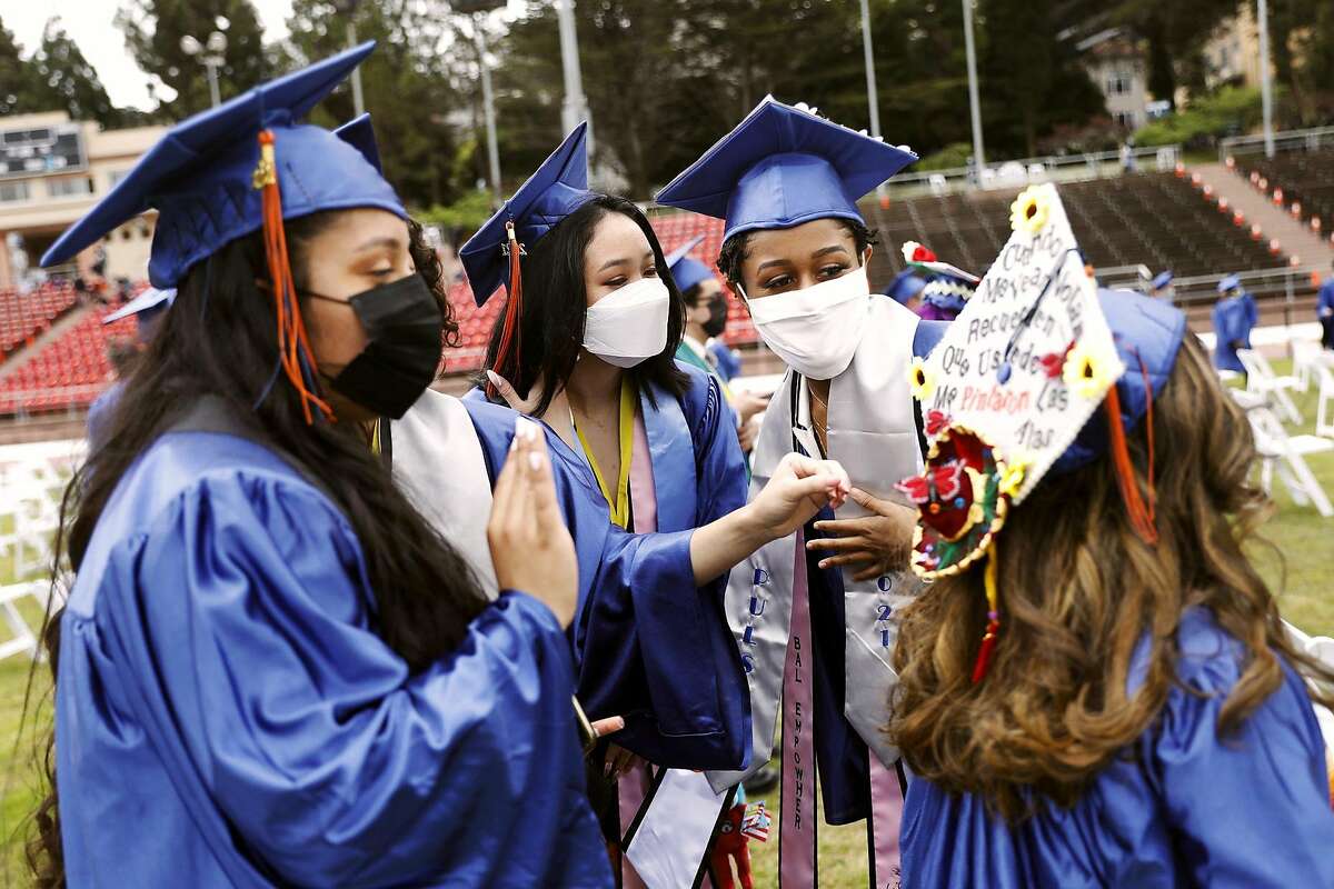 Marvely Tomas (from left), Wendy Huang and Pierce Whitney admire Valeria Serrano’s decorated cap before Balboa High School’s graduation ceremony at Kezar Stadium in San Francisco.