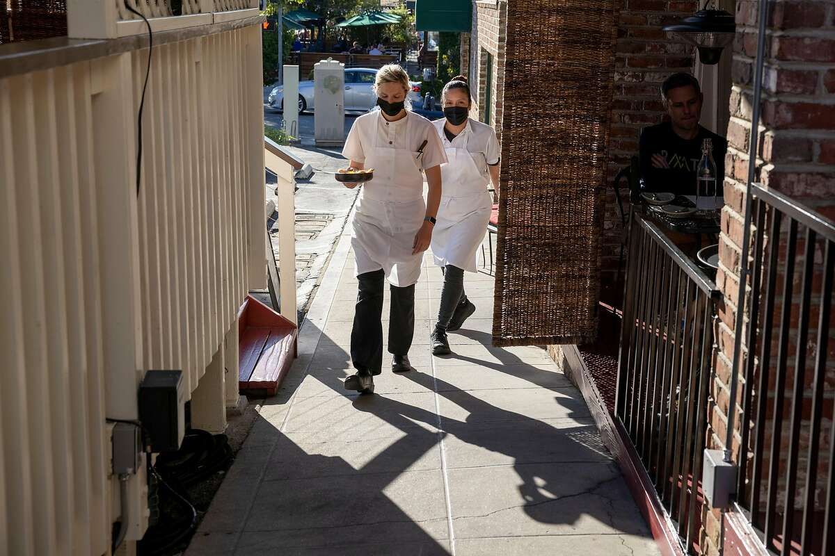Cooks Elisha Smiley (left) and Erika Morales bring plates to guests during dinner service at Flea Street Cafe in Menlo Park.