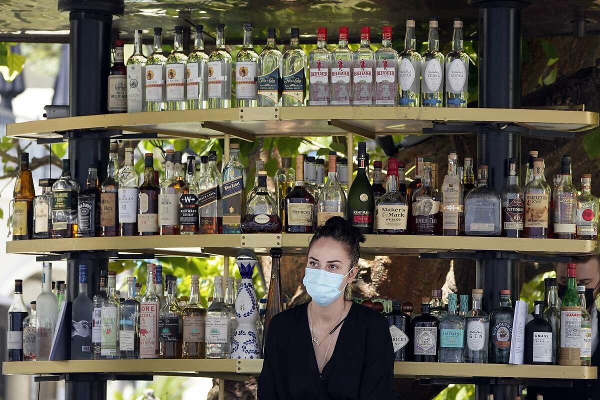 A bartender wears a mask while working at an outdoor bar at The Grove in Los Angeles. The standards board of California’s Division of Occupational Safety and Health, voted to loosen workplace mask rules on Thursday, but the new standards are still more strict than the CDC’s guidelines.