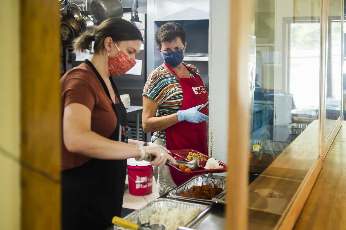 Volunteers MaryBeth Rentsch, left, and Laura Browne, center, load up a plate with hot food for a guest during the regular soup kitchen hours at Midland's Open Door Friday, June 4, 2021. (Katy Kildee/kkildee@mdn.net)