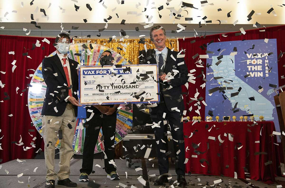 Gov. Gavin Newsom, state Sen. Richard Pan, left, and UC Davis assistant nurse manager Claudio Alvarado, center, hold a mock check as the state drew the first 15 winners to be awarded $50,000 for getting vaccinated against COVID-19 at the California Lottery on Friday in Sacramento.