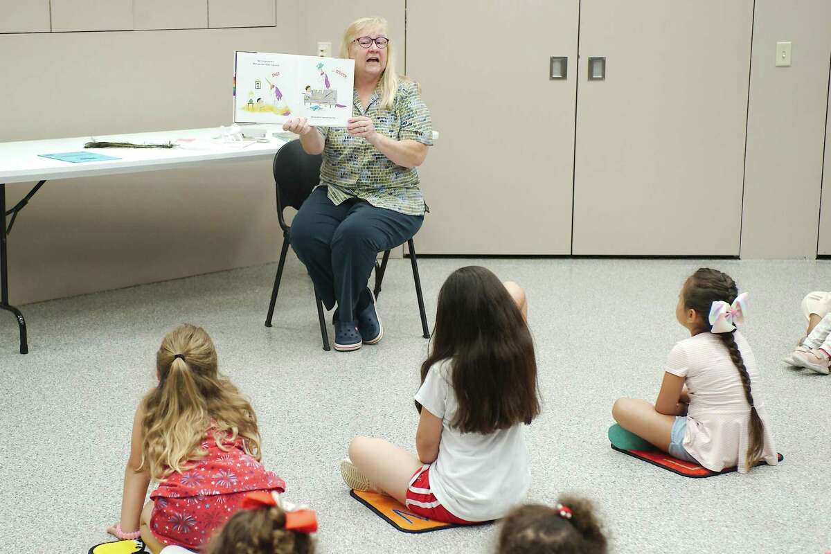 McKenzie Loosemore, Mia Zamarron, and Victoria Vargas listen as Fairmont Library Children's Librarian Leslie Guhl reads a story during family story time.