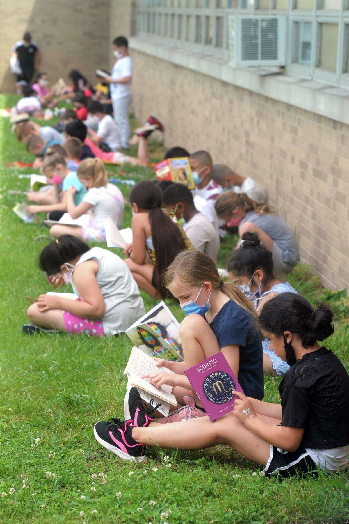 Students read in the shade of their school building on a sweltering morning as they take part in the kickoff event for the summer reading program at Long Hill School, in Shelton, Conn. June 8, 2021.