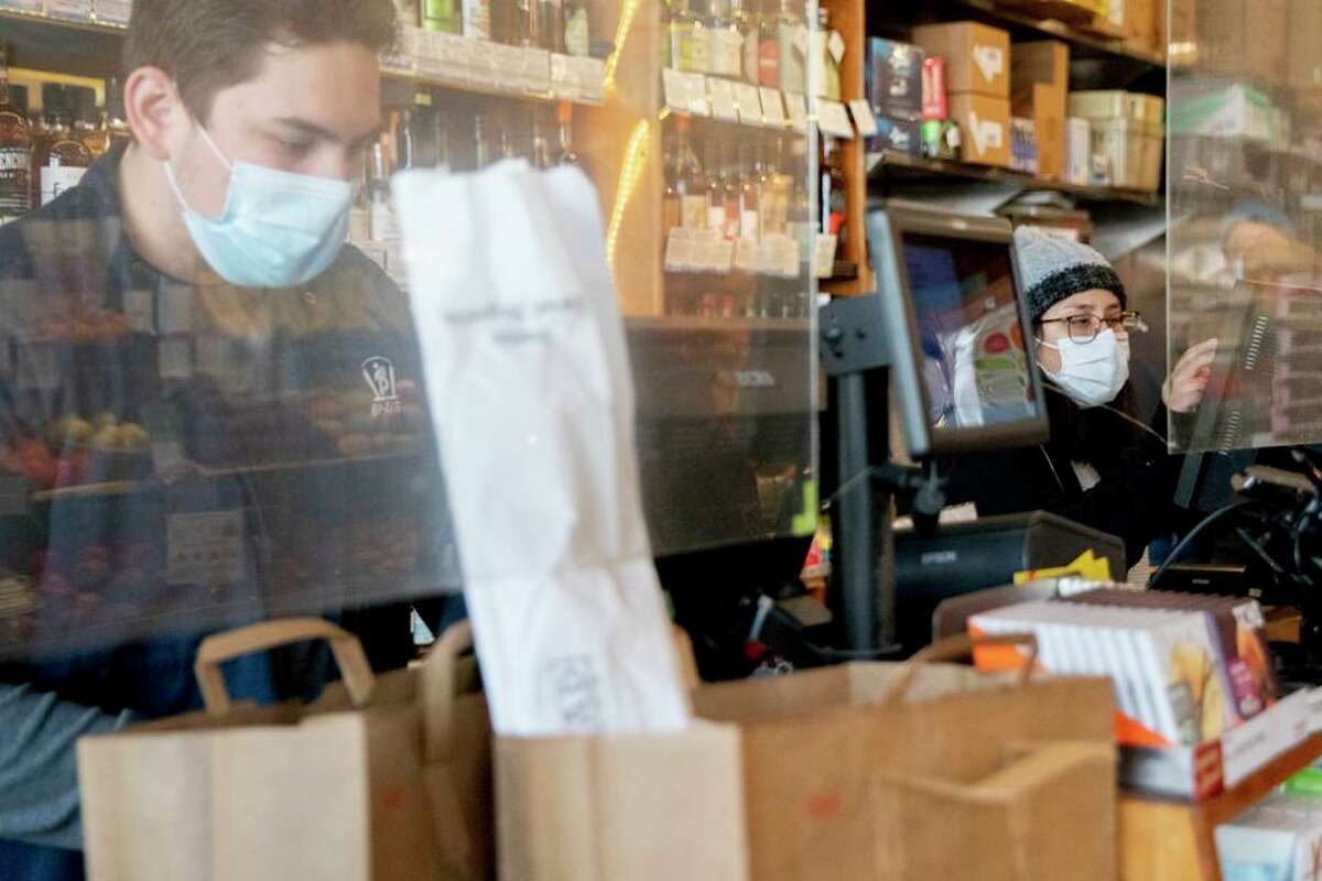 Employees wear masks and stand behind plexiglass barriers while assisting customers at Bi-Rite Market in the Mission District of San Francisco, on Nov. 20, 2020.