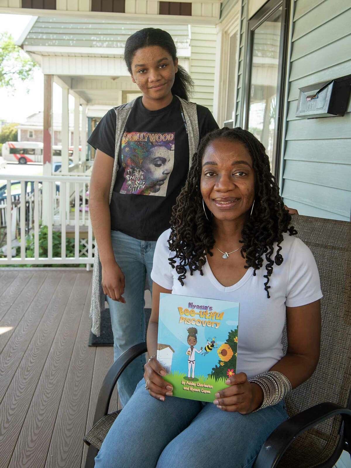Ashley Charleston holds her book while sitting on her porch next to her niece Nyasia Copes on Thursday, June 10, 2021 in Schenectady, N.Y. Charleston is a self-published Schenectady-based children's book author who wrote a story Nyasia's Bee-utiful Discovery, about her niece, Nyasia. (Lori Van Buren/Times Union)