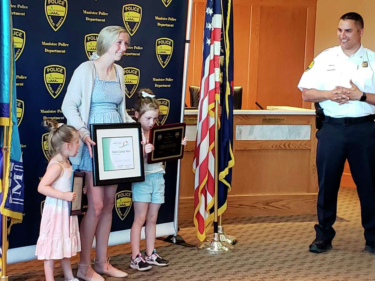 Alyssa Dewitt stands with daughters Cleo Knapp (left) and Briar Knapp after Manistee City Police Chief Josh Glass (right) presented her with several awards. Dewitt saved several children from a near drowning incident at First Street Beach last month. (Arielle Breen/News Advocate)