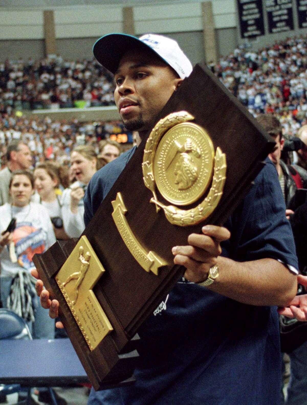Connecticut basketball team co-captain Ricky Moore carries the winner's trophy during a rally for the team on the UConn campus in Storrs, Conn. Tuesday, March 30, 1999. The UConn men's team defeated Duke 77-74 to win the NCAA Division I men's basketball championship Monday, March 29, 1999. (AP Photo/Carla Cataldi)