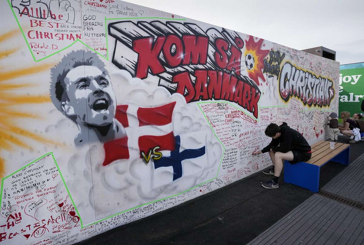 People writing well wishes at a graffiti for Danish player Christian Eriksen on a wall at the fanzone in Copenhagen, Denmark, Monday, June 14, 2021. Eriksen remains in hospital after he collapsed on the pitch during the European Championship game against Finland on Saturday and needed CPR from medical staff before regaining consciousness. (AP Photo/Martin Meissner)