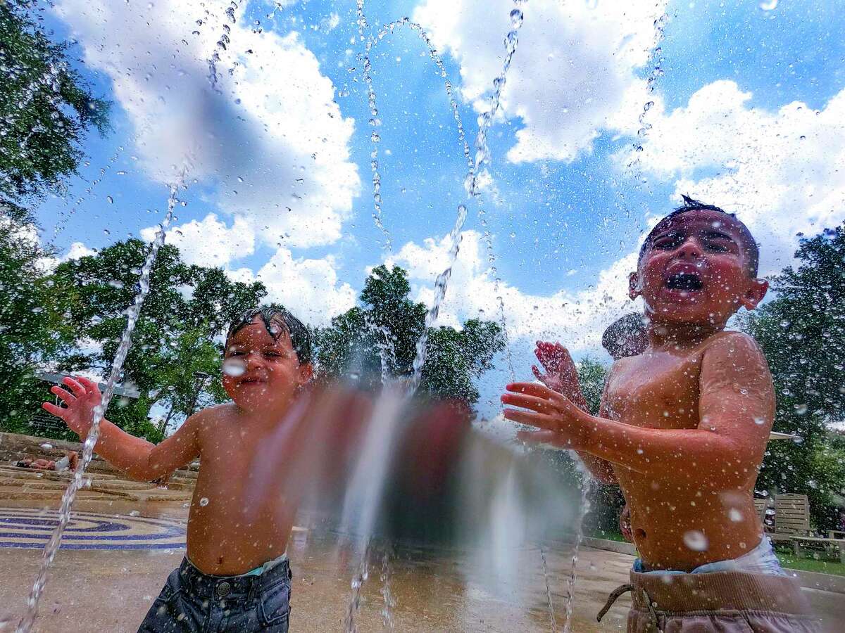 Malaki, left, and King Berlanga cool off in the heat at Yanaguana Garden in Hemisfair Park on Monday. With temperatures and concern for the state’s power grid rising, the city said it would begin opening cooling centers.