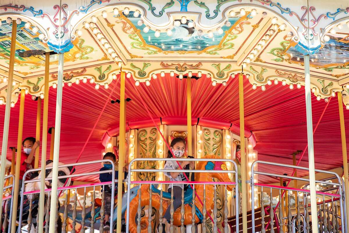 (Fom left) Jack Robinson, 7, Dom Robinson, 5, and Gianna Robinson, 9, wear masks before choosing a seat on the carousel at Pier 39 on the first day of lifted COVID-19 restrictions in San Francisco, Calif. Tuesday, June 15, 2021. California lifted nearly all of its pandemic restrictions at 12:01 a.m. on Tuesday, June 15, a date marking a key milestone in reopening efforts for the state and the San Francisco Bay Area.