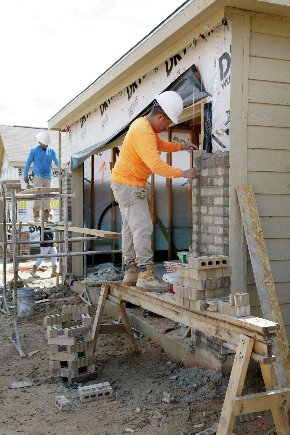 Construction workers lay bricks on the exteriors of new houses by LGI Homes along Lost Lantern Drive in a new section of the Bauer Landing sub-division Thursday, June 3, 2021 in Hockley, TX.