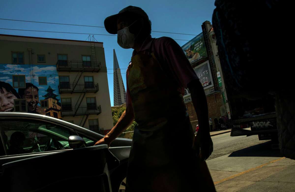 A worker walks along Stockton Street as the Transamerica Pyramid is seen in the background in San Francisco on Tuesday. After 15 months of battling the COVID-19 pandemic, California lifted most of its public health restrictions Tuesday.