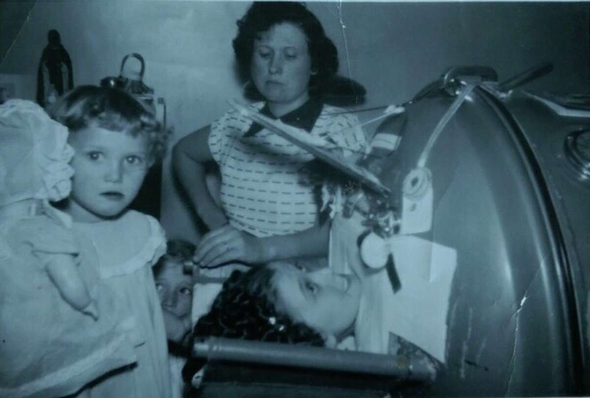 Bonny Kehm's mother, seen in the foreground with her doll, stands next to her sister Lillian in an iron lung. Their mother stands in the background.