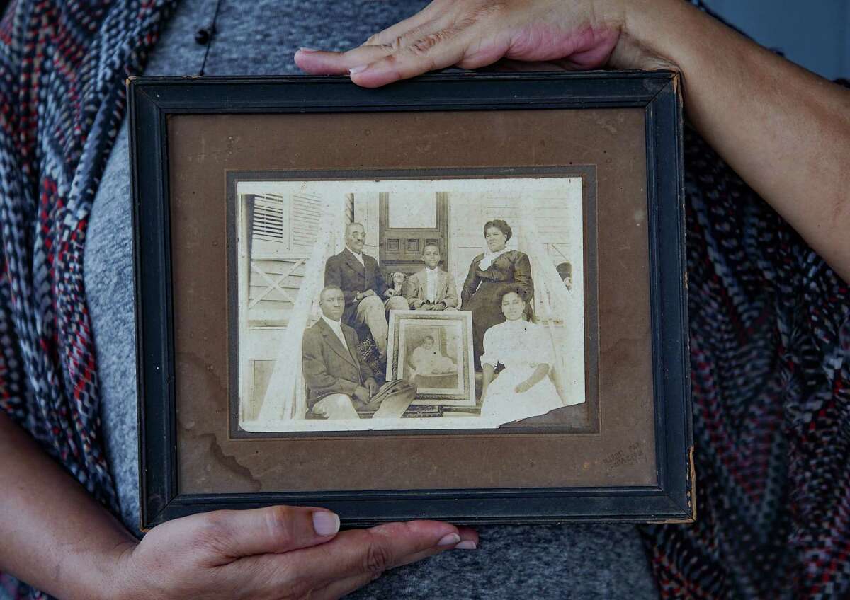 June Pulliam holds a photo of her ancestors sitting in front of the home she still lives in, in Galveston on Friday, May 28, 2021. Pulliam's family migrated to Galveston in 1865, when her great-grandfather, Horace Scull (top left in the photo) was five years old.