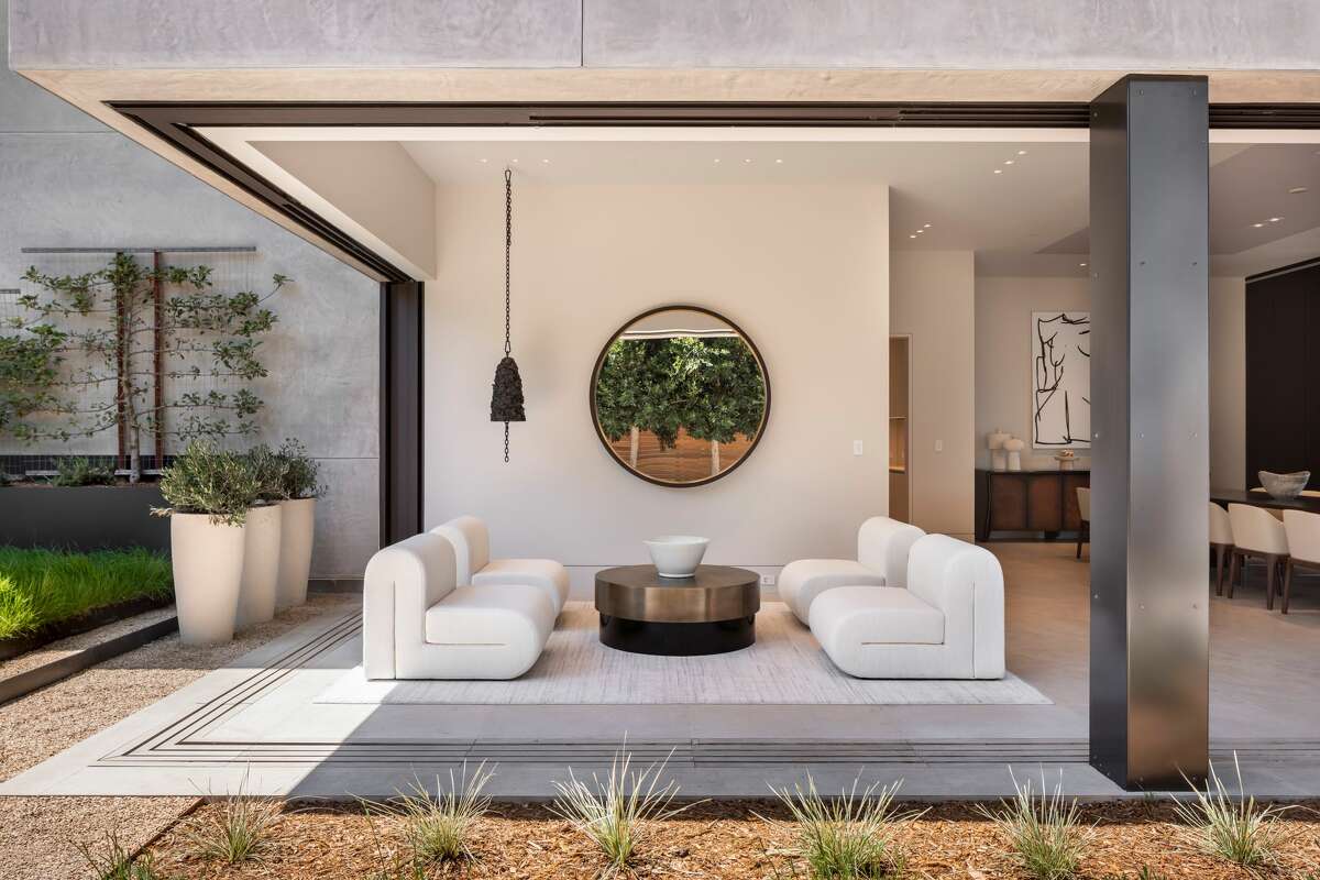 This lounge area looks out at a rear garden with stone hardscape, fire pit, lawn and outdoor kitchen.