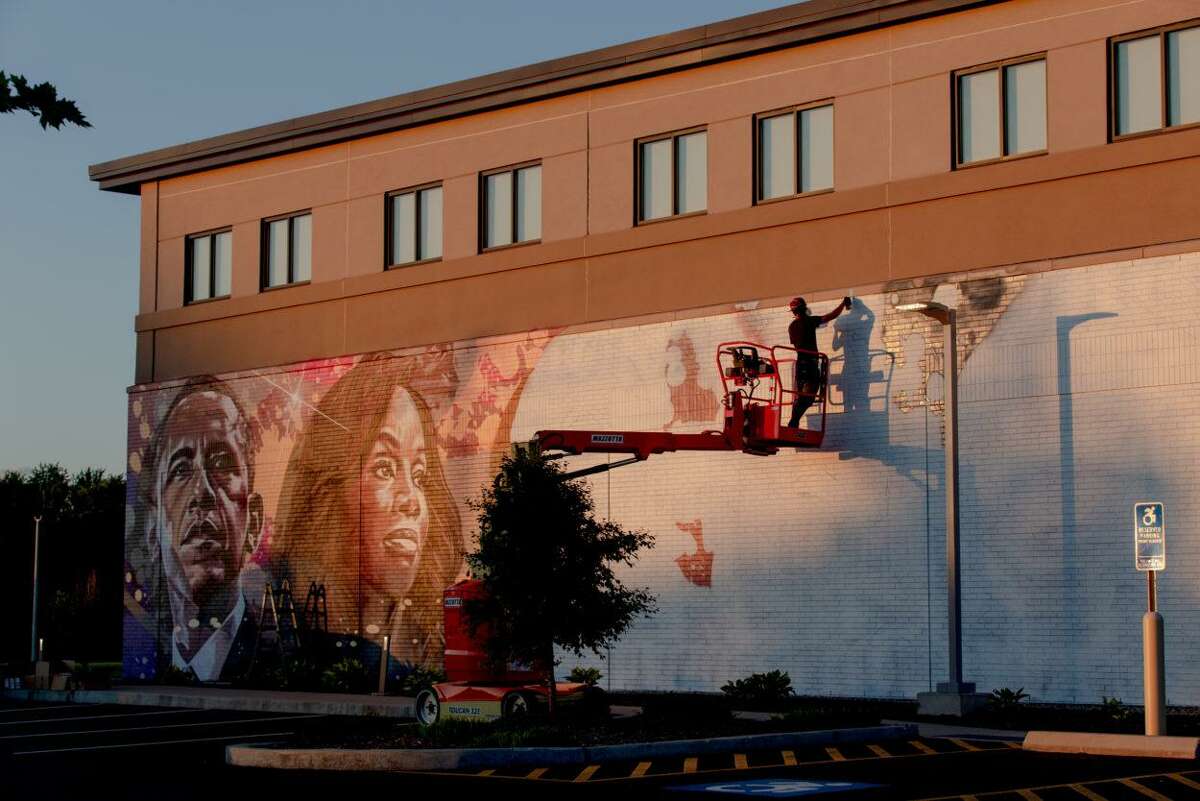 Ryan Christenson, of North Haven, who goes by ARCY, paints the wall of Alvin and Beatrice Wood Human Services Center, a community center in Bloomfield. Barack Obama, left, and Anika Rose, a Bloomfield native, are painted on the wall.