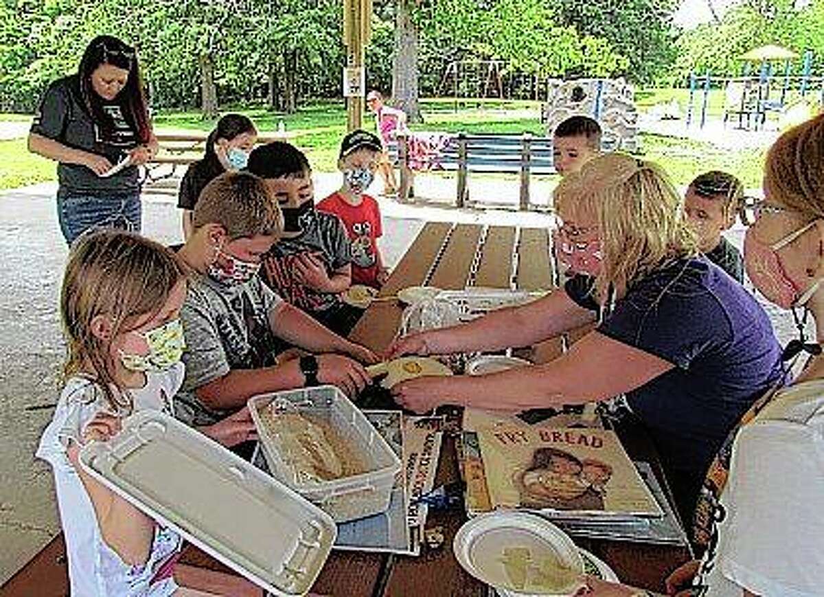 Nadia Kahl (right), children’s co-librarian for Carlinville Public Library, helps participants in the library’s summer reading program with a crafts project earlier this month at Loveless Park. Children up to age 10 are eligible to participate in the program.