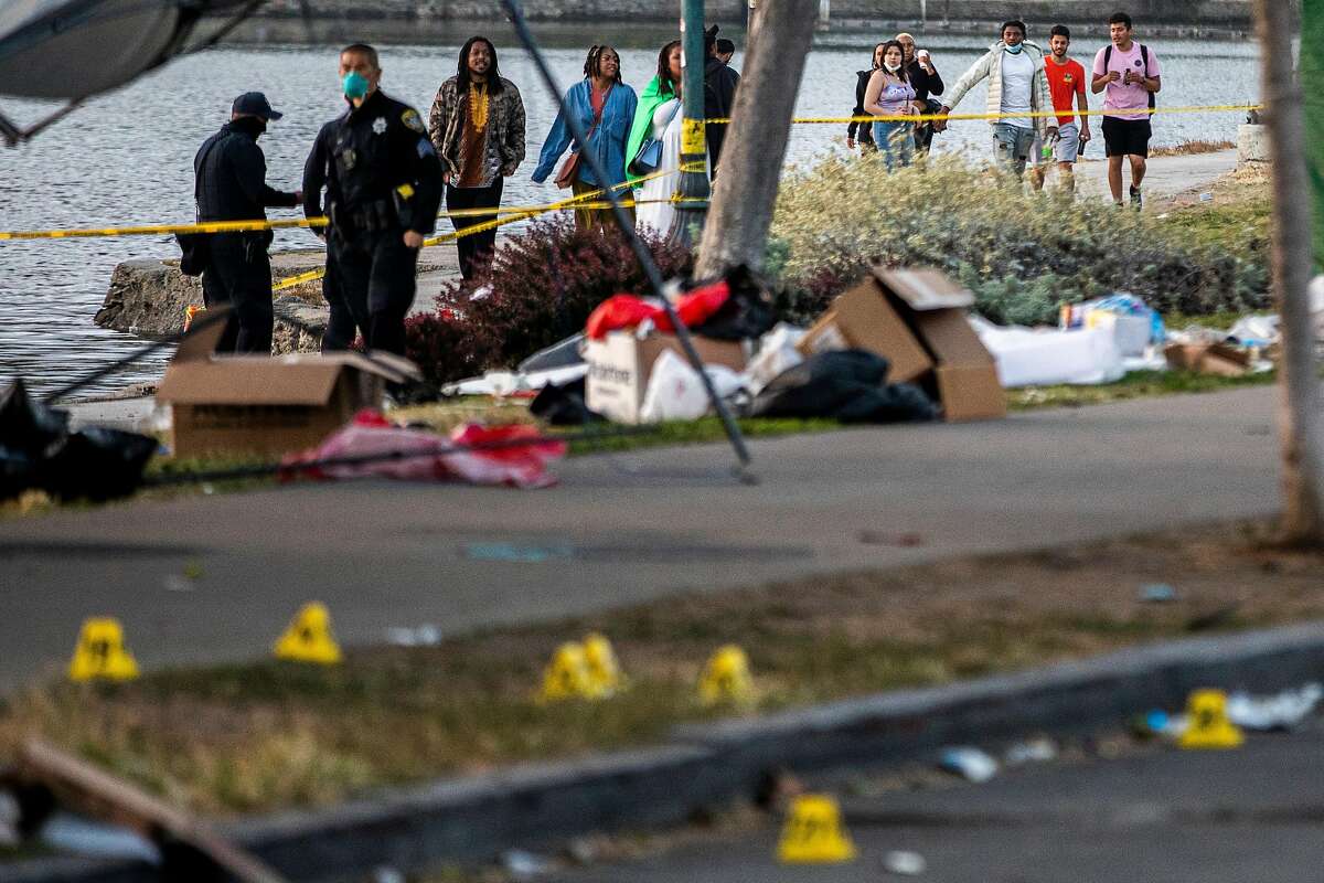 People behind police tape watch as police investigate the scene of a fatal shooting along Lakeshore Avenue at Brooklyn Avenue, Saturday, June 19, 2021, in Oakland, Calif. Oakland police said Monday that evidence suggests the shooting was tied to a feud between two rival gangs or groups in San Francisco.