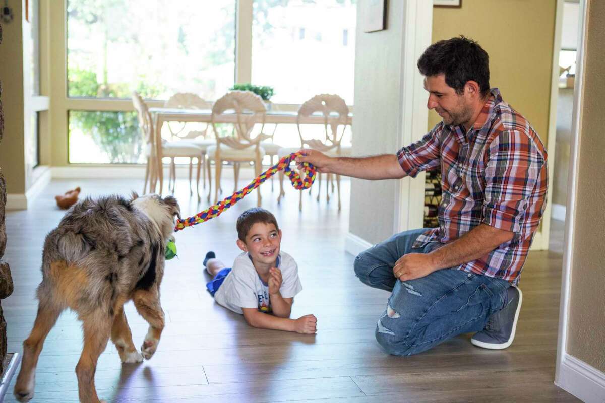 Alan Kornfeld (center) and his father, Shay Kornfeld, play with the family dog, Bullet, on the floor of the family house in Walnut Creek. Shay and his wife cashed out some of their Dogecoin earnings to buy a $1,500 dog at one point, and they like to joke that Bullet is now a $18,000 puppy.