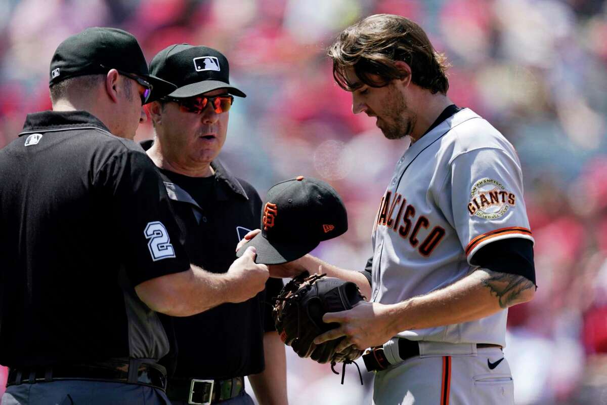 San Francisco Giants starting pitcher Kevin Gausman, right, has his hat, glove and belt checked by umpires after the fourth inning of a baseball game against the Los Angeles Angels Wednesday, June 23, 2021, in Anaheim, Calif. (AP Photo/Mark J. Terrill)