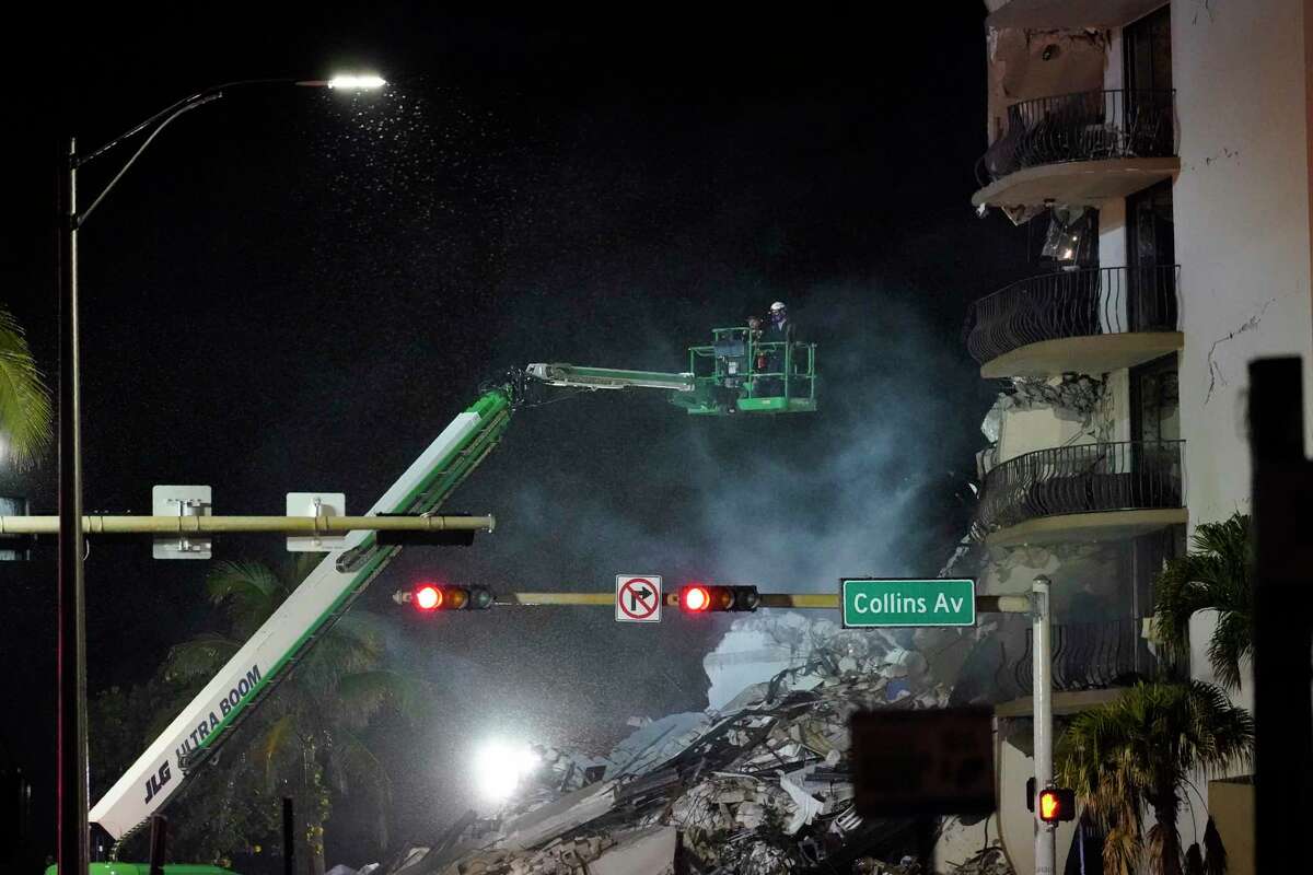 Workers ride in a lift as smoke rises off the rubble where a wing of a 12-story beachfront condo building collapsed, late on Thursday, June 24, 2021, in the Surfside area of Miami.