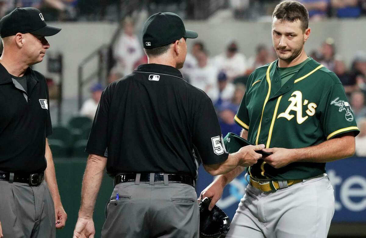 Oakland Athletics relief pitcher Burch Smith has his glove and hat checked by the umpires after he pitches in the sixth inning against the Texas Rangers in a baseball game Tuesday, June 22, 2021, in Arlington, Texas. (AP Photo/Louis DeLuca)