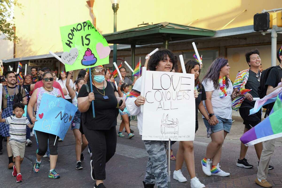 Members hold signs in support of the LGBTQ+ community as they walk in the Pride Parade on Iturbide St. on June 26.
