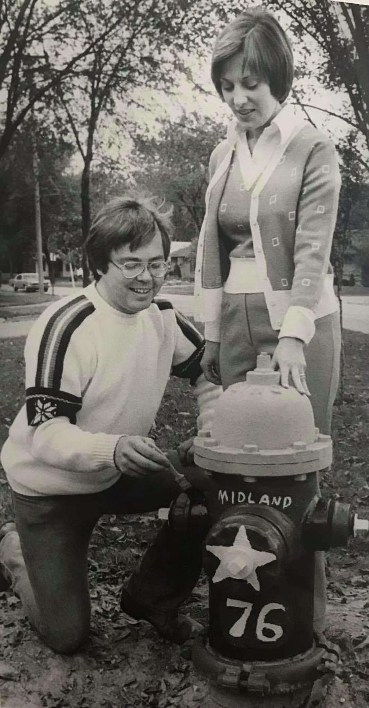 Stephen J. Engelken, administrative assistant for the Midland Community Affairs Council, paints the first hydrant in advance of the Bicentennial Fire Hydrant Painting Contest sponsored by Women's Optimist League. Looking on is Leslie Causgrove, head of the league. October 1975