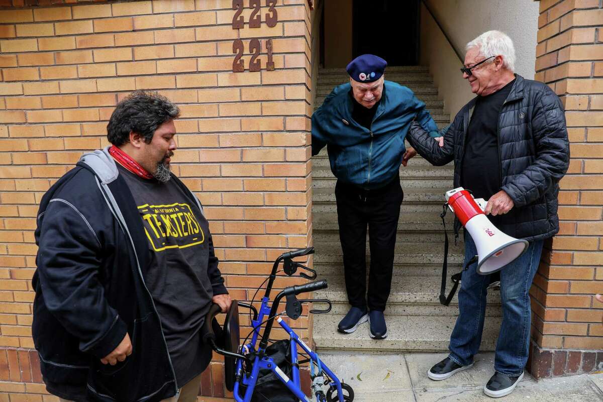Ruben Bustillos, Teamsters Local 70, Oakland, left, holds Allan Baird’s walker as Baird is aided by his friend Cleve Jones, right, down the stairs after Jones led a march from Harvey Milk Plaza to Baird's home in San Francisco.