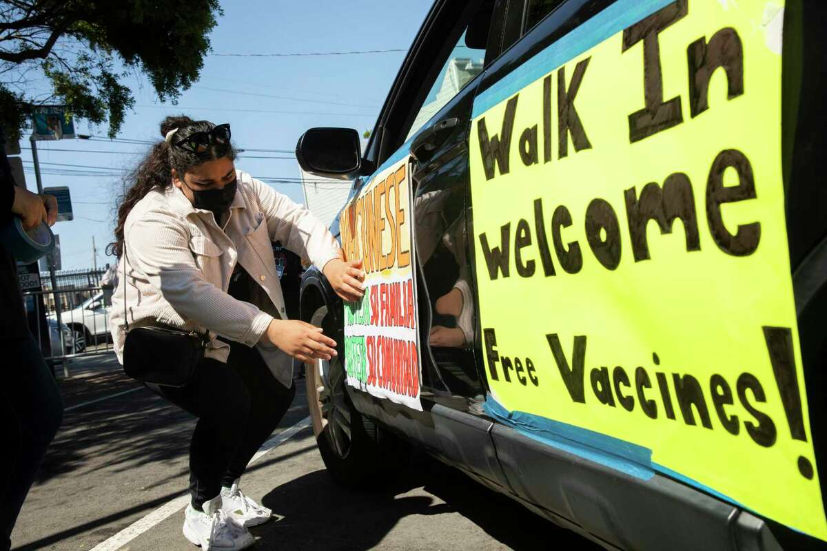 Sehar Fatima tapes signs to a roaming vehicle before heading out to do community outreach at a community pop-up vaccine site in San Francisco.