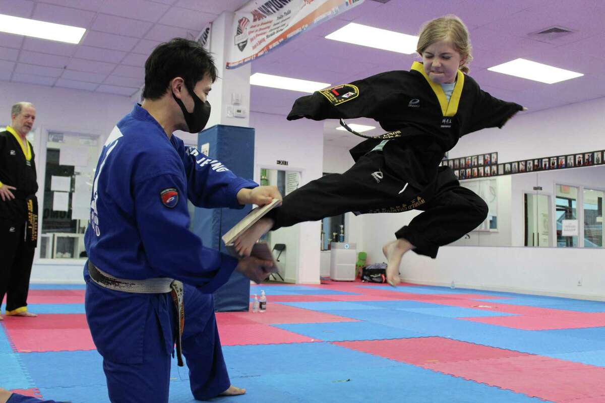 Ten-year-old Sofia Cluney snaps a wooden board after flying through mid-air at the World Champion Taekwondo dojo in Ridgefield. She was assisted by master Wooyeol Jeong as her father, Stephen, looked on. The Cluneys are the first in the dojo’s history to have four black belts within their family.