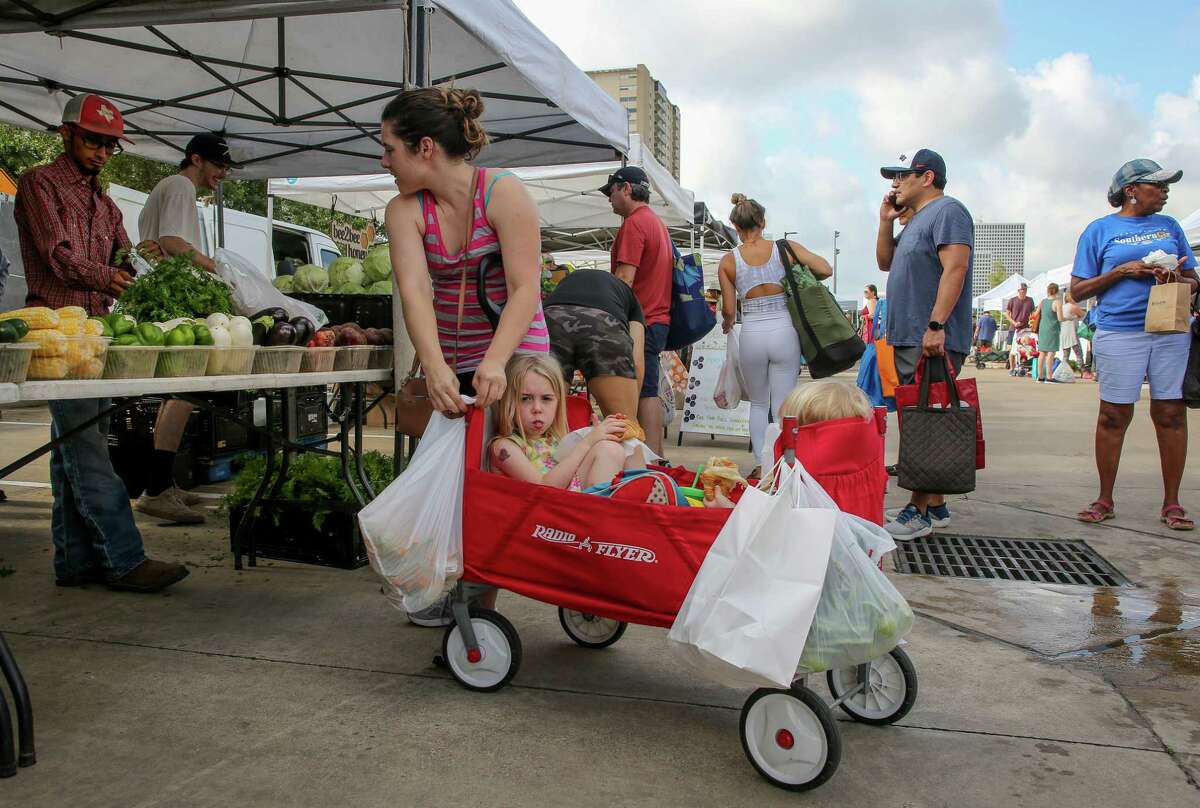 Elise Lorensen hangs a bag of produce to a four-wheel cart while shopping at Urban Harvest Farmers Market - which is located at 2752 Buffalo Speedway - with her children Mia and Blake on Saturday, June 12, 2021, in Houston.