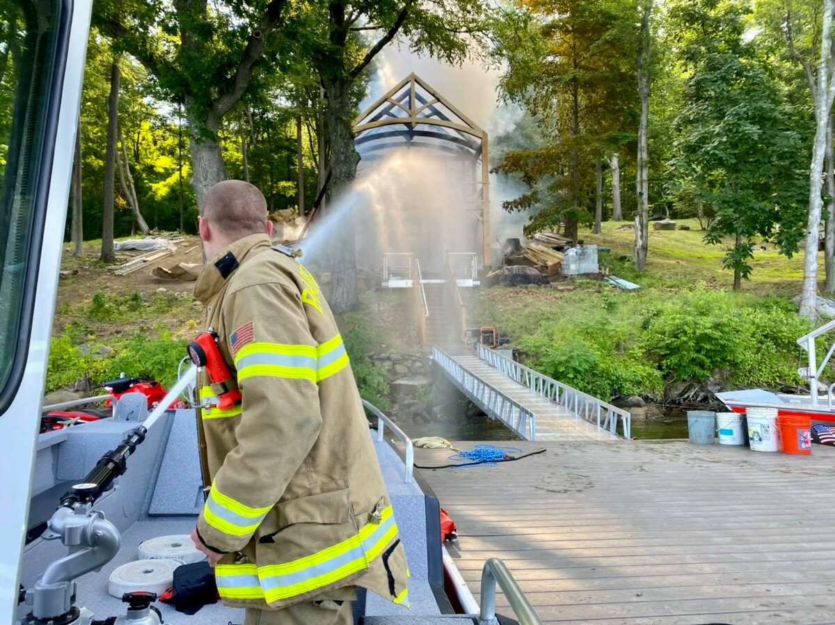 Firefighters douse water on a lakefront structure that caught fire in New Fairfield, Conn., the morning of June 29, 2021.