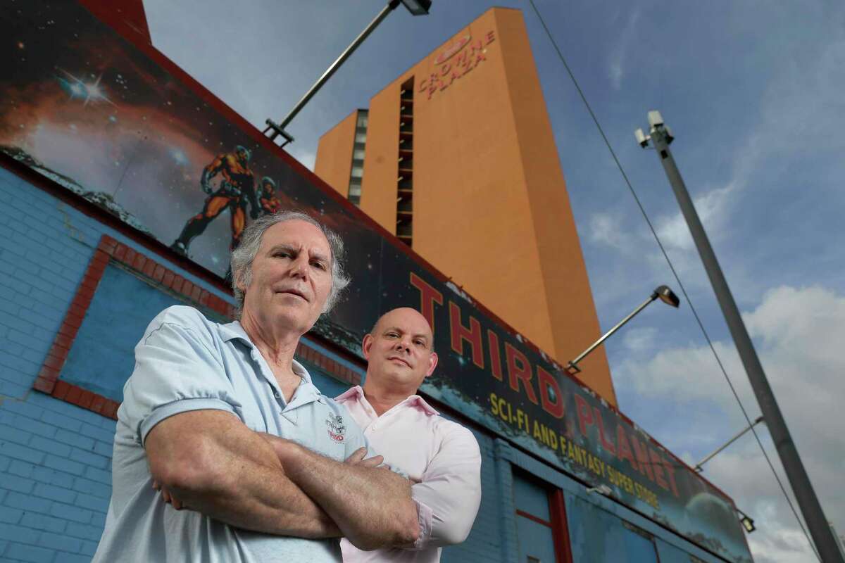 T.J. Johnson, left, and attorney Cris Feldman, right, outside the Third Planet Sci-Fi Superstore, a comics shop owned by Johnson that has been around for 45 years, under the balconies of the adjacent Crown Plaza Hotel Tuesday, June 29, 2021 in Houston, TX. The two have filed a lawsuit against the hotel accusing it of allowing its tenants to throw projectiles on their roof of the comics shop for years.