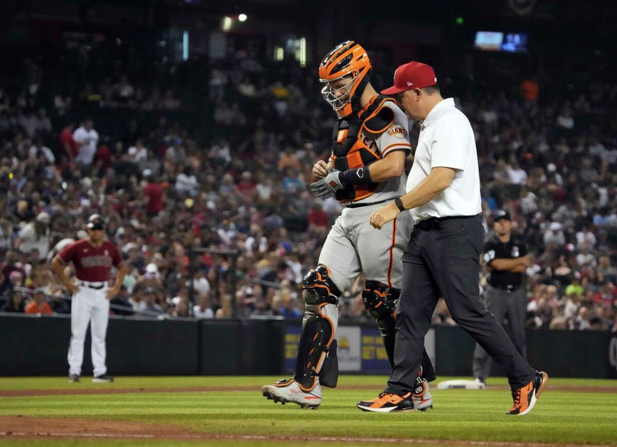 San Francisco Giants catcher Buster Posey leaves the game with a trainer after getting hit with the ball in the sixth inning of a baseball game against the Arizona Diamondbacks, Sunday, July 4, 2021, in Phoenix. (AP Photo/Rick Scuteri)