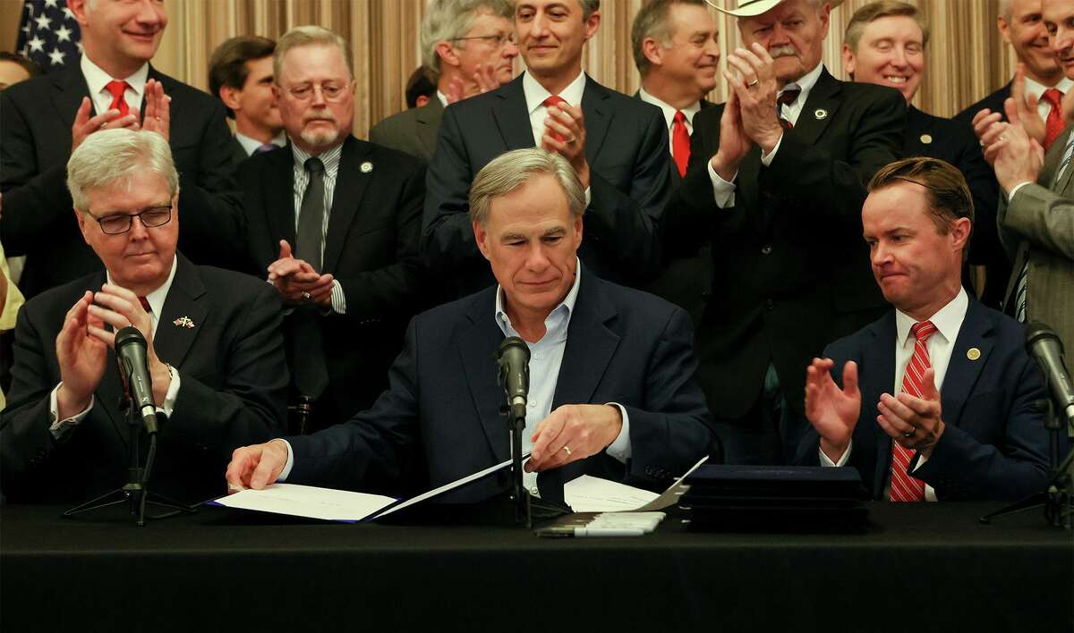 Texas Governor Greg Abbott, center, seated next to Lieutenant Governor Dan Patrick, left, and Speaker Dade Phelan prepares to sign a "constitutional carry" bill allowing Texans to carry handguns without a permit along with several other pieces of legislation relating to the Second Amendment in Alamo Hall at the Alamo on Thursday, June 17, 2021. The bills are scheduled to take effect on September 1.