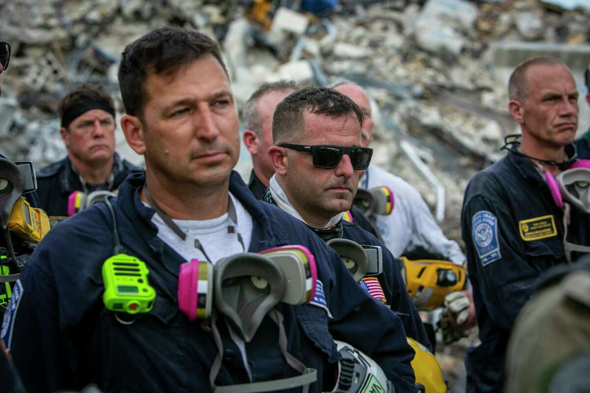 Members of a search and rescue team stand in front of the rubble that once was Champlain Towers South during a prayer ceremony in Surfside, Fla., Wednesday, July 7, 2021. Members of search and rescue teams and Miami-Dade Fire rescue along with police and workers who have been working at the site of the collapse gathered for a moment of prayer and silence next to the collapsed tower. (Jose A Iglesias/Miami Herald via AP)