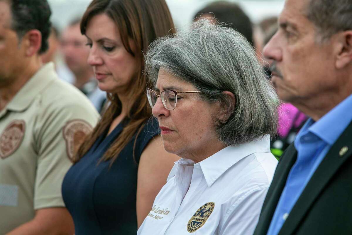 Miami-Dade County Mayor, Daniella Levine Cava, center, stands with other officials in from of the rubble that once was Champlain Towers South in Surfside, Fla., Wednesday, July 7, 2021. Members of search and rescue teams and Miami-Dade Fire rescue along with police and workers who have been working at the site of the collapse gathered for a moment of prayer and silence next to the collapsed tower. (Jose A Iglesias/Miami Herald via AP)