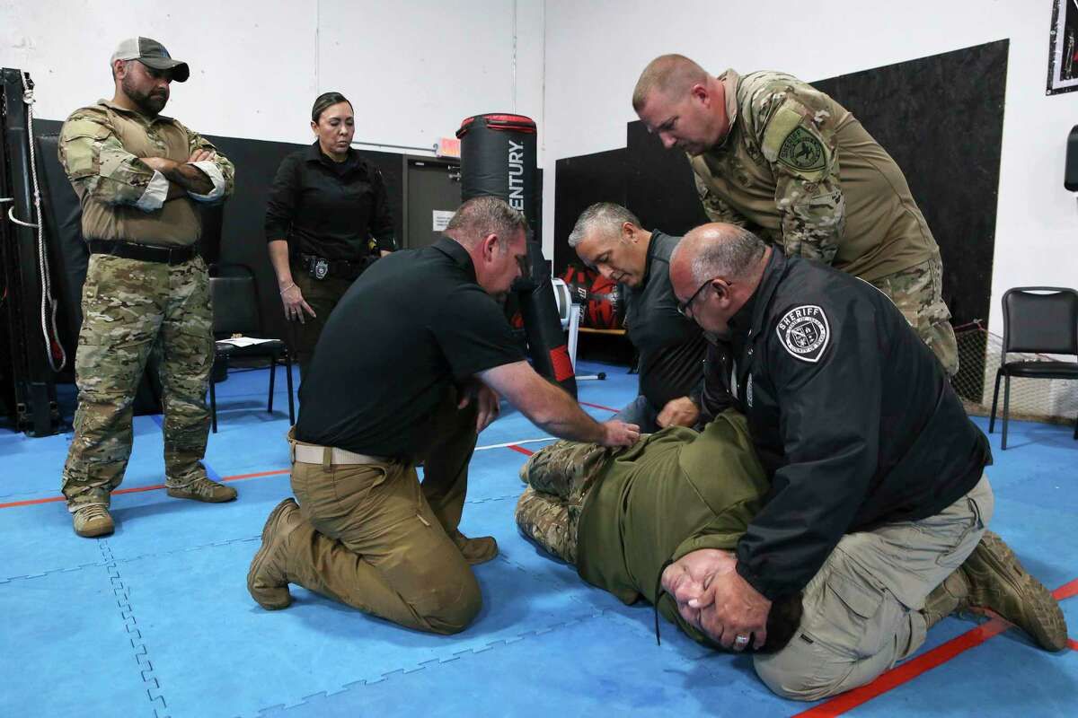 Instructor Joshua Thomas (left, kneeling) oversees Bexar County Sheriff’s Office deputies as they practice a restraint technique that’s part of the CALM Approach, which was developed by a retired San Antonio police officer’s training company called Con10gency Consultants. The methodology has received a national certification and is being adopted in other states.