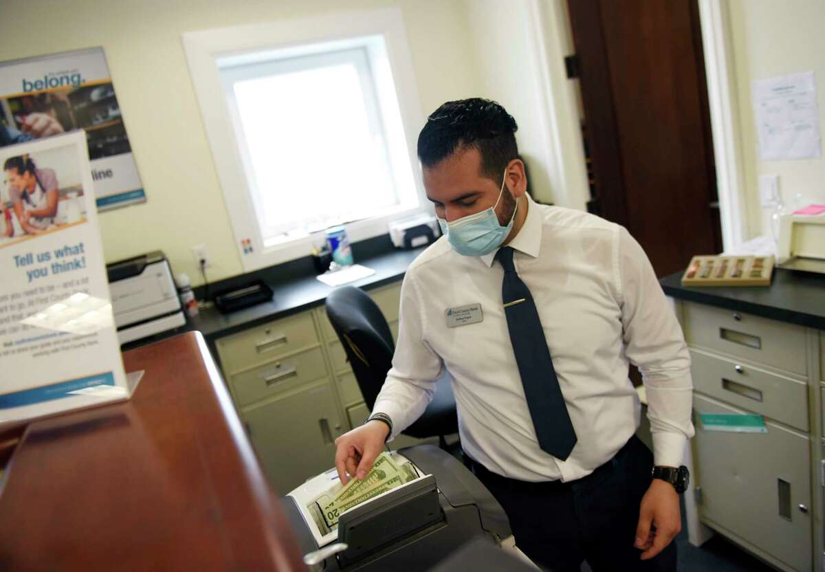 Bank teller Joshua Seput runs a stack of bills through the money machine at First County Bank in Stamford, Conn. Thursday, July 8, 2021.