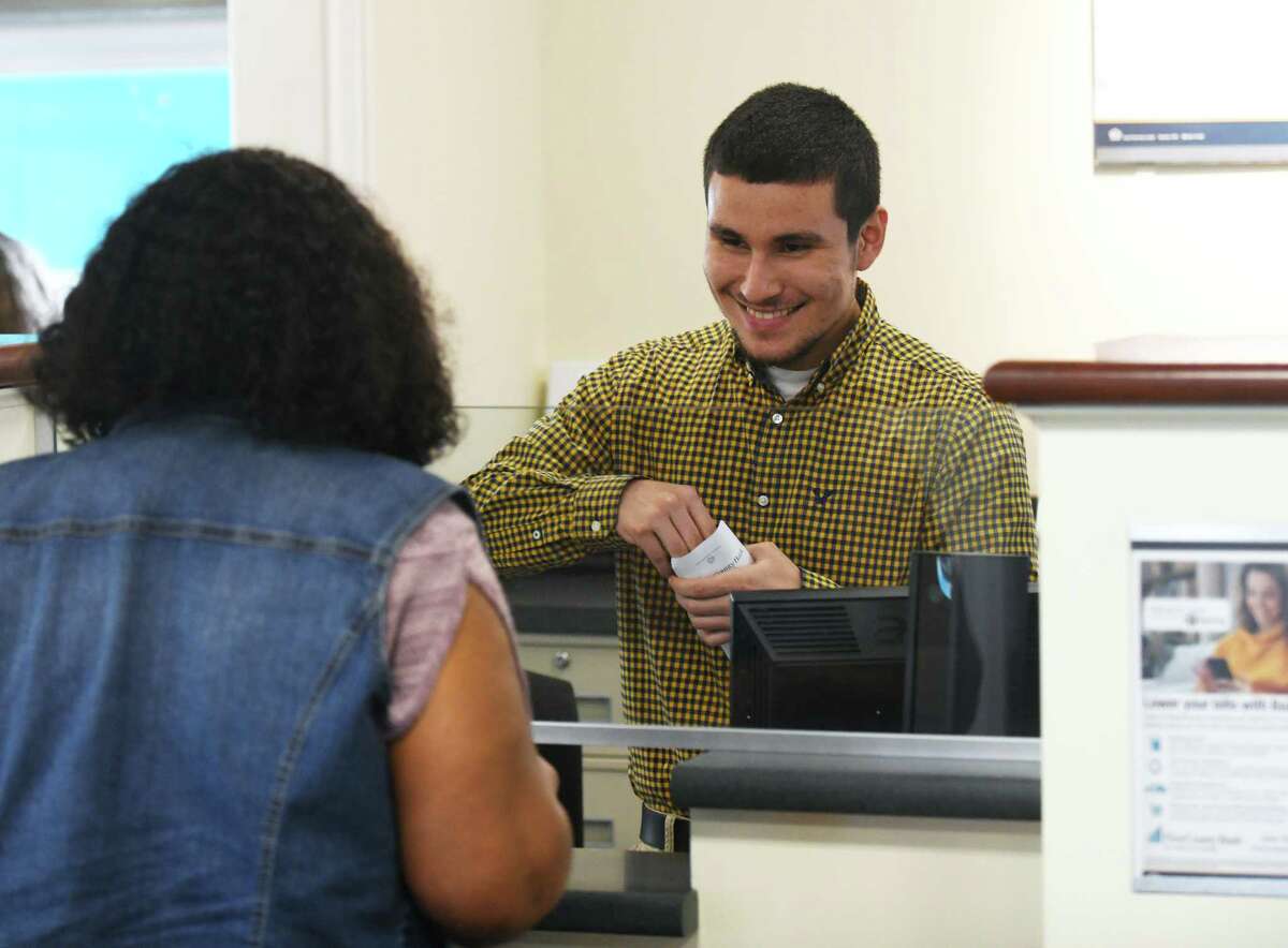 Bank teller Kelvin Recinos assists a customer at First County Bank in Stamford, Conn. Thursday, July 8, 2021.